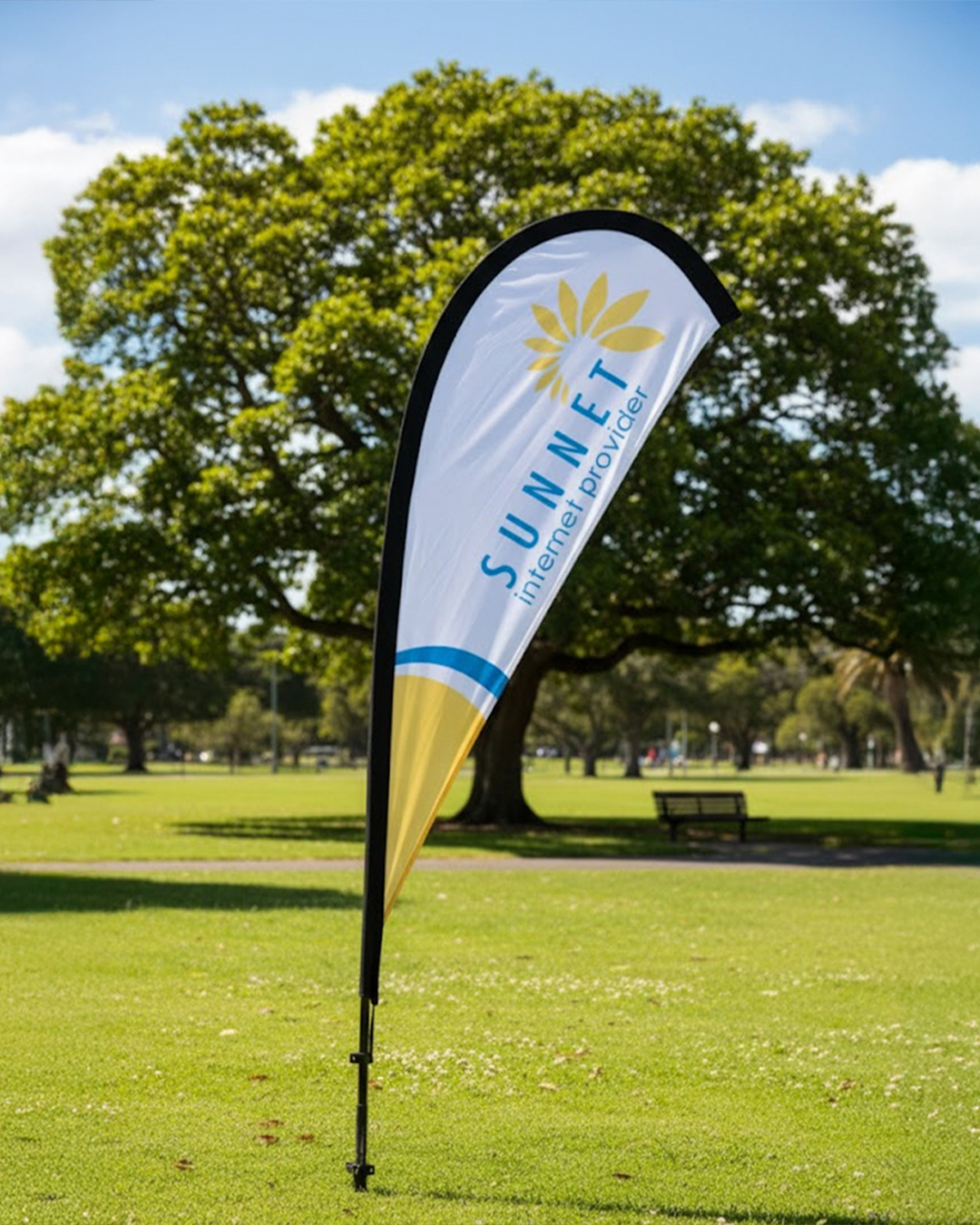 a curved teardrop banner with printed branding staked into grass at an outdoor site on a sunny day