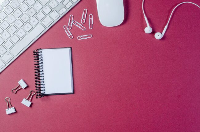 flat lay of a designer at a desktop computer with business card mockups visible on screen and a selection of printed card samples arranged a