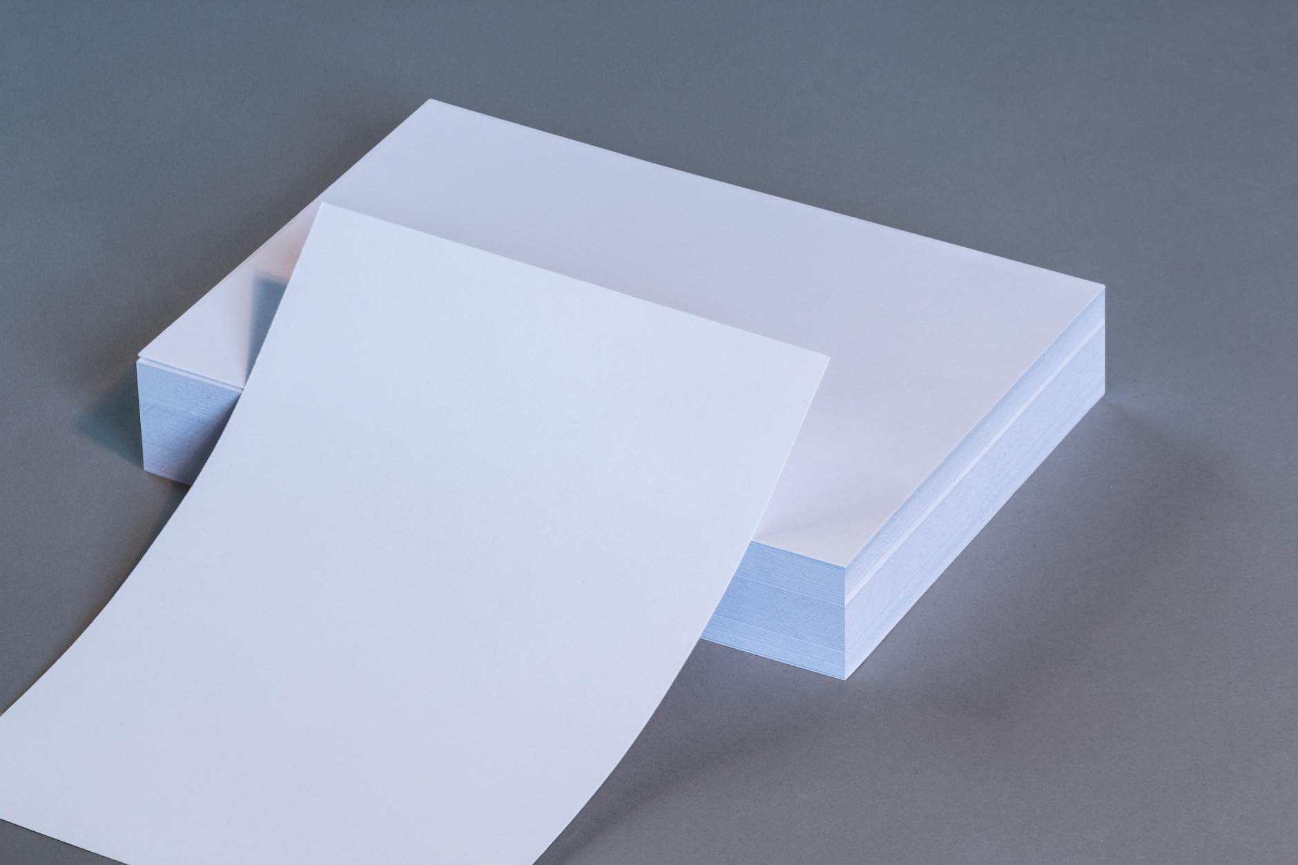 neat stack of freshly printed standard business cards on a white office desk, clean minimal design visible on the top card, with a coffee cu
