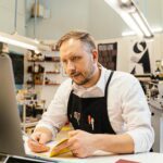 small business owner reviewing freshly printed business cards at a timber desk with notebook and coffee nearby