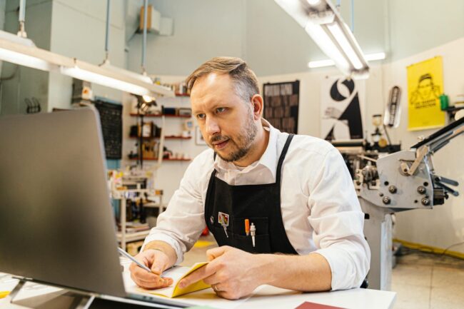 small business owner reviewing freshly printed business cards at a timber desk with notebook and coffee nearby