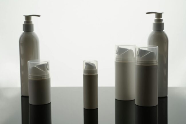 Overhead flat-lay of glass skincare bottles and kraft mailer pouches with clear transparent product labels applied, showing the no-label loo