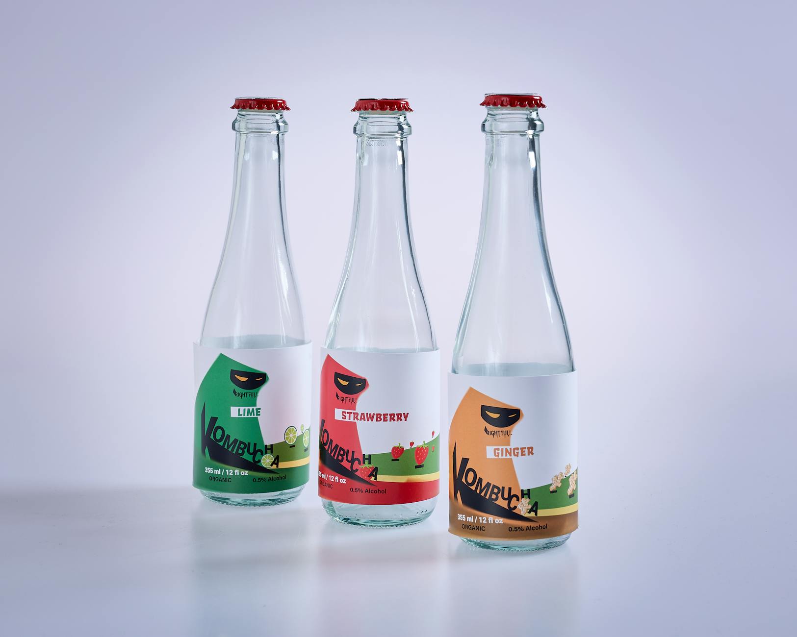 Clear transparent labels applied to three glass kombucha bottles, showing the see-through no-label effect where the drink is visible through the label