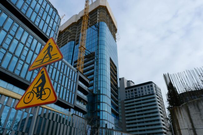 Construction site project signboard on hoarding fence showing builder company branding and project details, clear daylight, Australian urban