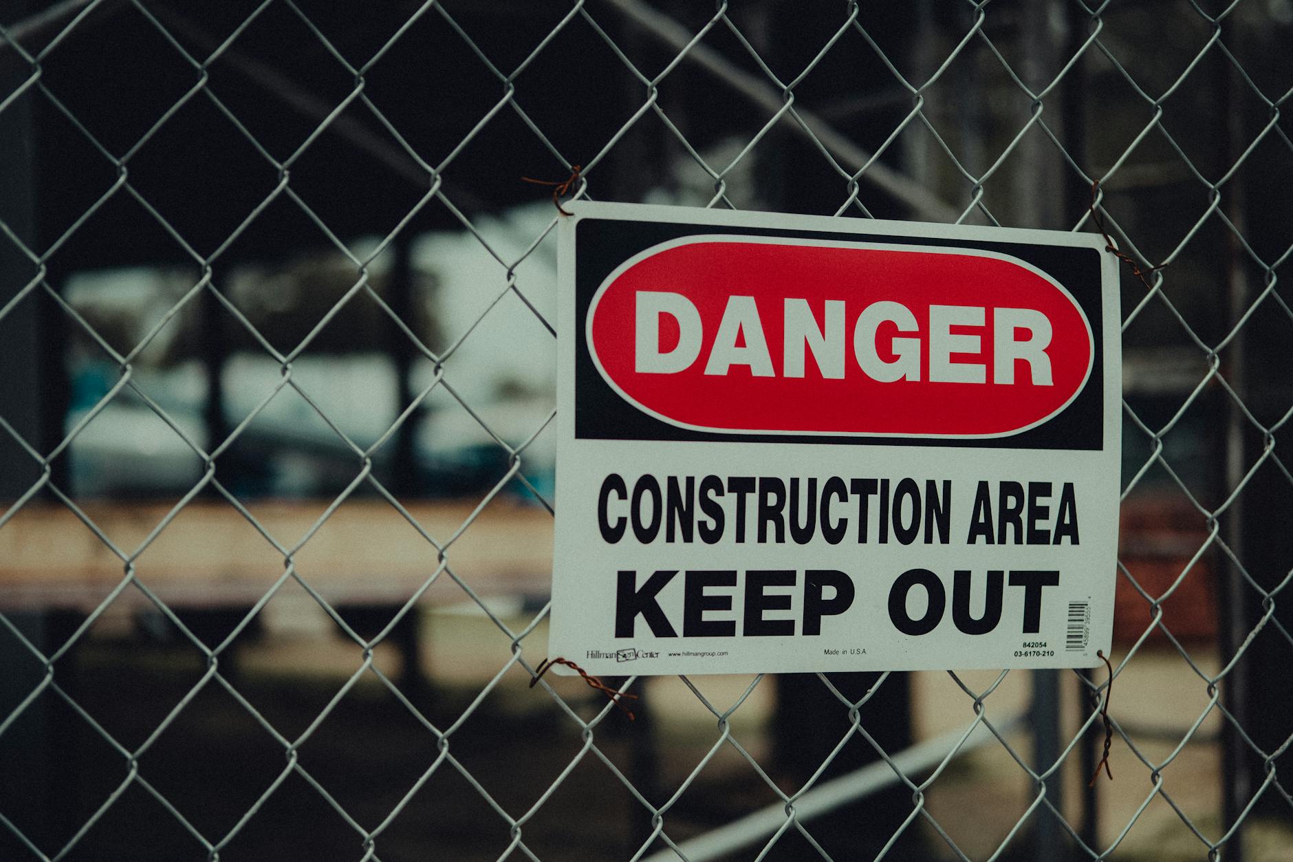 H-frame mounted corflute safety signs at a construction site entrance showing mandatory PPE requirements, set against a hoarding fence