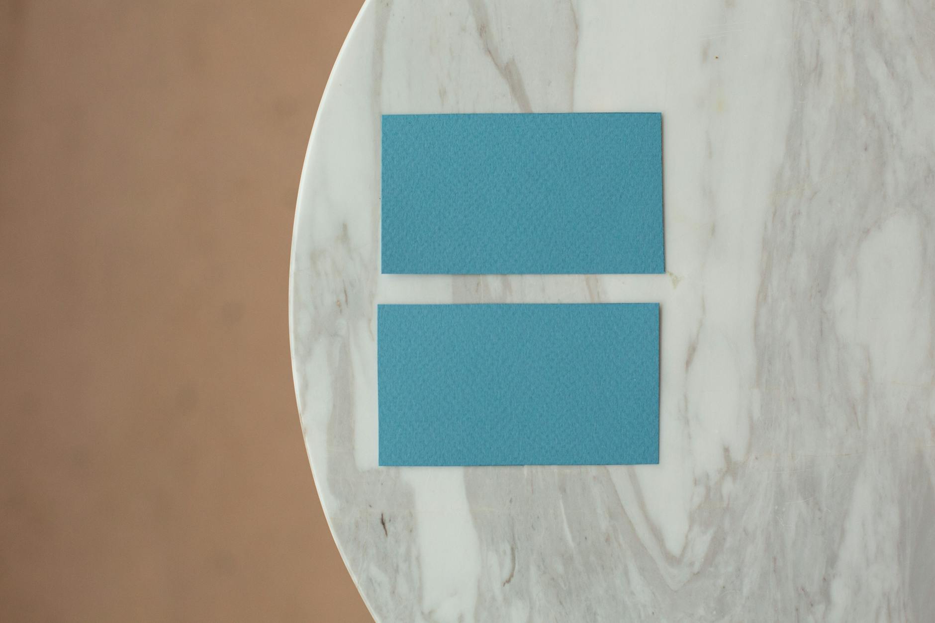 Two business cards photographed face-up and face-down on a timber desk, the white front showing clean sans-serif black typography, the rever