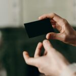 A close-up of a matte black business card with a holographic foil logo catching the light, showing the rainbow colour shift against the dark