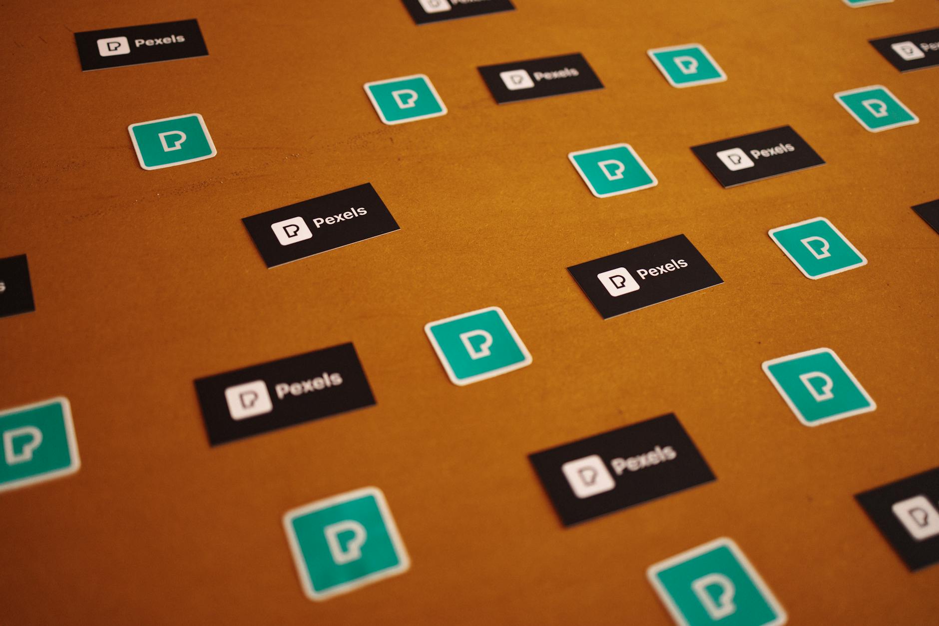 A branded sticker kit laid out in a kraft paper envelope on a light timber desk, showing three die-cut stickers in complementary brand colou