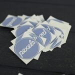 Flat lay of custom-printed logo stickers in various shapes and finishes arranged on a clean white surface with a coffee cup and kraft paper