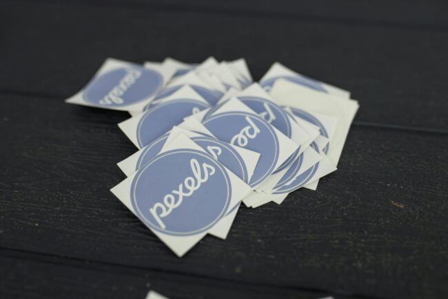 Flat lay of custom-printed logo stickers in various shapes and finishes arranged on a clean white surface with a coffee cup and kraft paper
