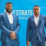 Two professionals in matching blue suits standing in front of a branded fabric backdrop at a corporate event, showcasing how stretch fabric media walls anchor presenter photo opportunities.