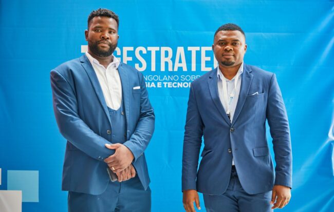 Two professionals in matching blue suits standing in front of a branded fabric backdrop at a corporate event, showcasing how stretch fabric media walls anchor presenter photo opportunities.