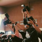 Press photographer scrum at a high-profile media event, cameras raised at presenter height — the working distance media wall sizing accounts for.