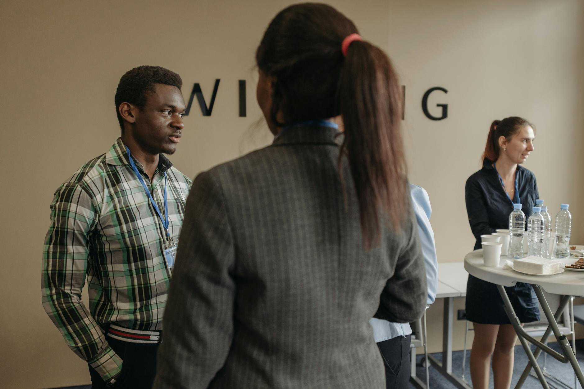 two professionals at an industry networking event exchanging business cards across a table with name badges visible in the background
