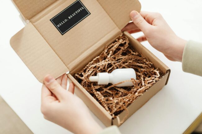 Overhead flatlay of a branded product launch unboxing box open on a light timber surface, showing a custom die-cut sticker pack, tissue pape