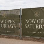 A perforated mesh banner beside a solid vinyl banner mounted on a fence outdoors, comparing the two outdoor banner materials for wind.