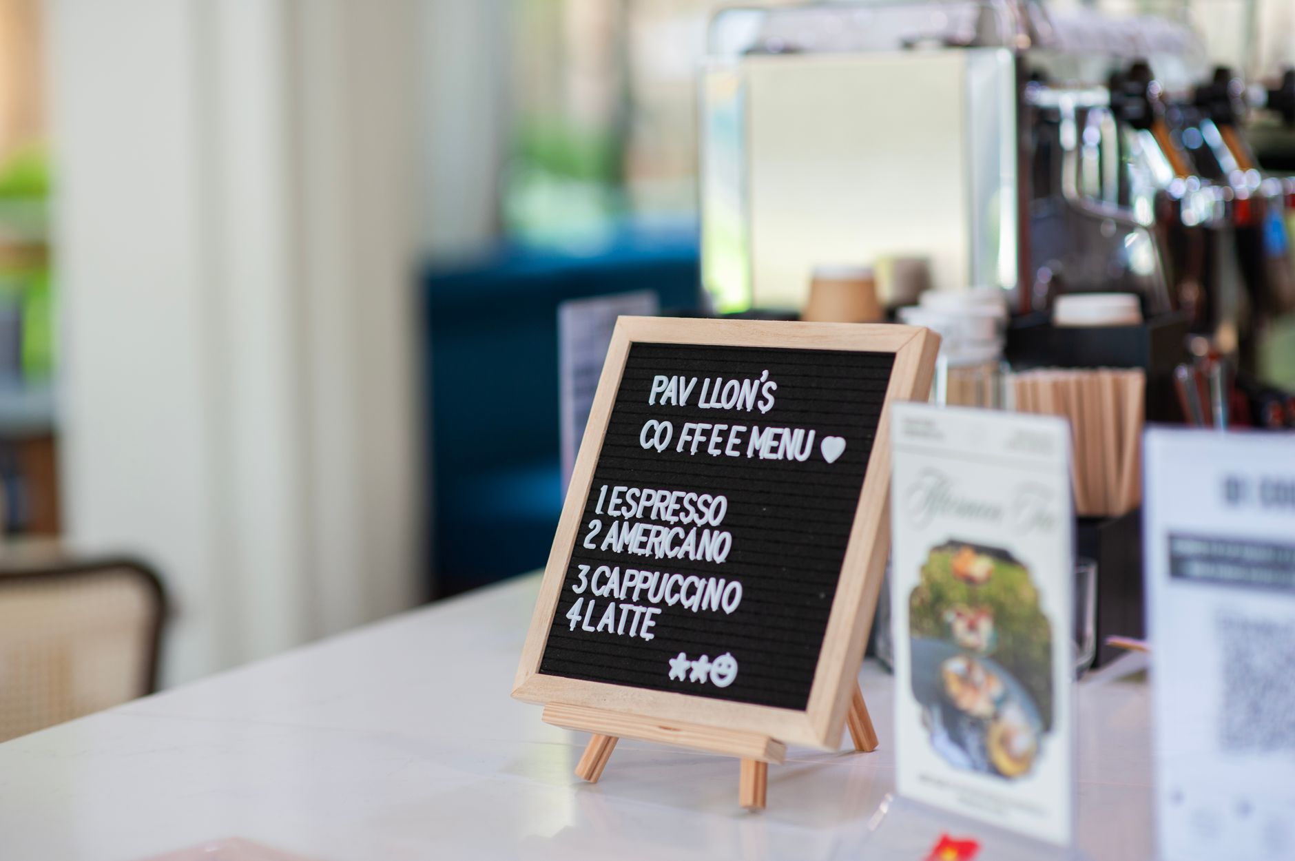 A5 laminated cafe menu displayed in a clear acrylic counter stand next to a barista machine, showing a clean menu layout with coffee