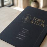 Close-up of a dark menu with gold foil and white-ink printing catching the light, showing premium foil and white-ink menu finishes.