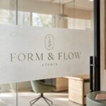 A glass office partition with frosted privacy film carrying a boutique wordmark, comparing one-way window film and frosted decals for office privacy.
