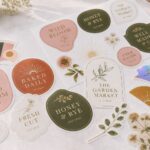 An editorial flatlay spread of varied boutique die-cut stickers, holographic, botanical, geometric, retro and typographic, illustrating 2026 sticker trends.