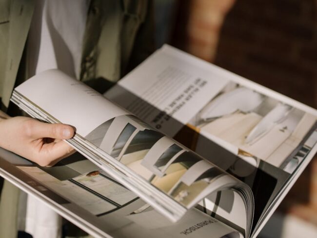 Hands turning the glossy printed pages of a magazine style catalogue
