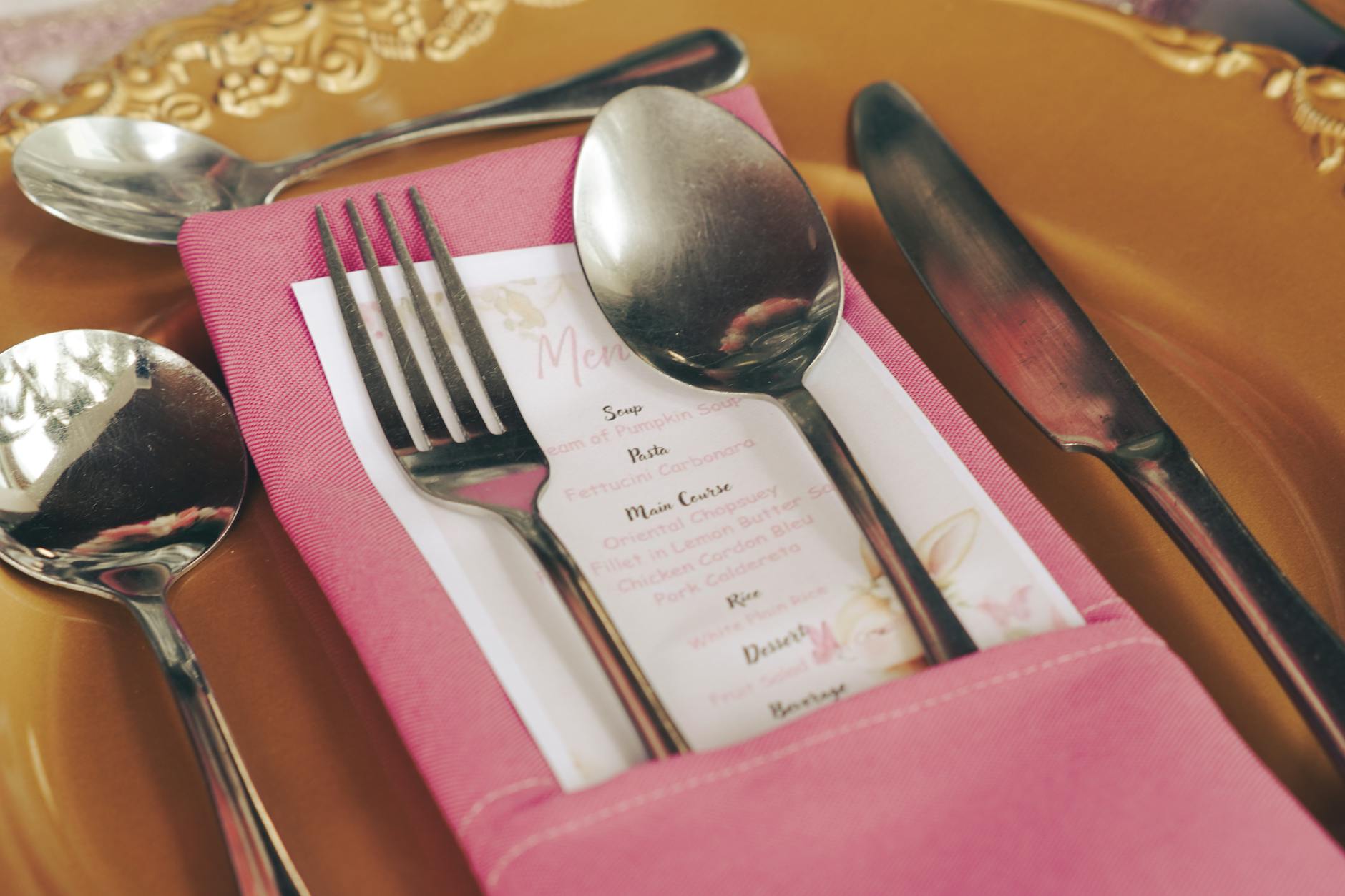 Close-up of a foil-printed DL wine menu lying on a dark timber table. Gold foil logo at the top catches the light, with full-colour wine