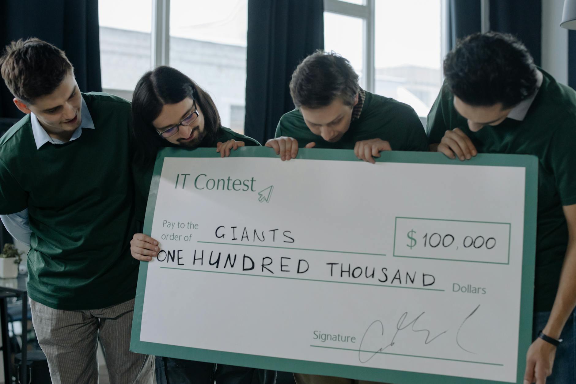 Close-up of a printed novelty cheque on rigid board showing full layout with logo, payee field, amount in numerals and words, and signature