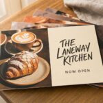 Fan of rectangular restaurant marketing postcards with appetising food-led designs on a neutral surface, used to drive dining foot traffic.