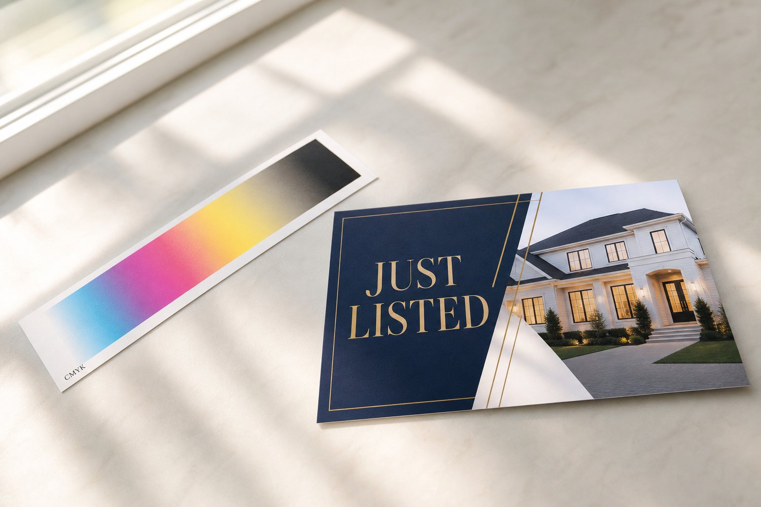 Slim printed process-colour bar beside a rectangular postcard on a neutral surface, illustrating CMYK versus RGB colour mode for printing.