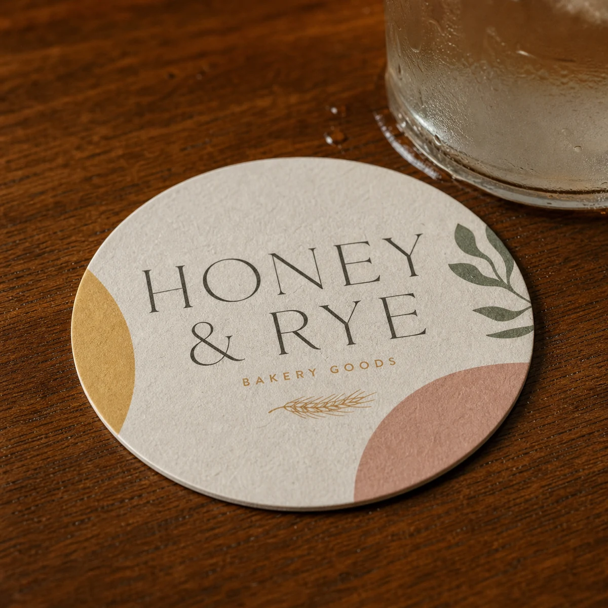 Close-up of a single round branded coaster on a polished timber bar with a frosted glass leaving a faint condensation ring, showing the matte absorbent beermat texture
