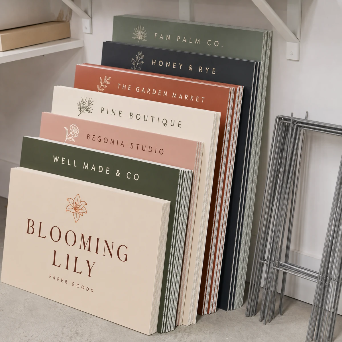 A stack of flat corflute signs stored upright in a clean dry storage room with a bundle of H-stakes leaning beside them, fluted cut edges visible