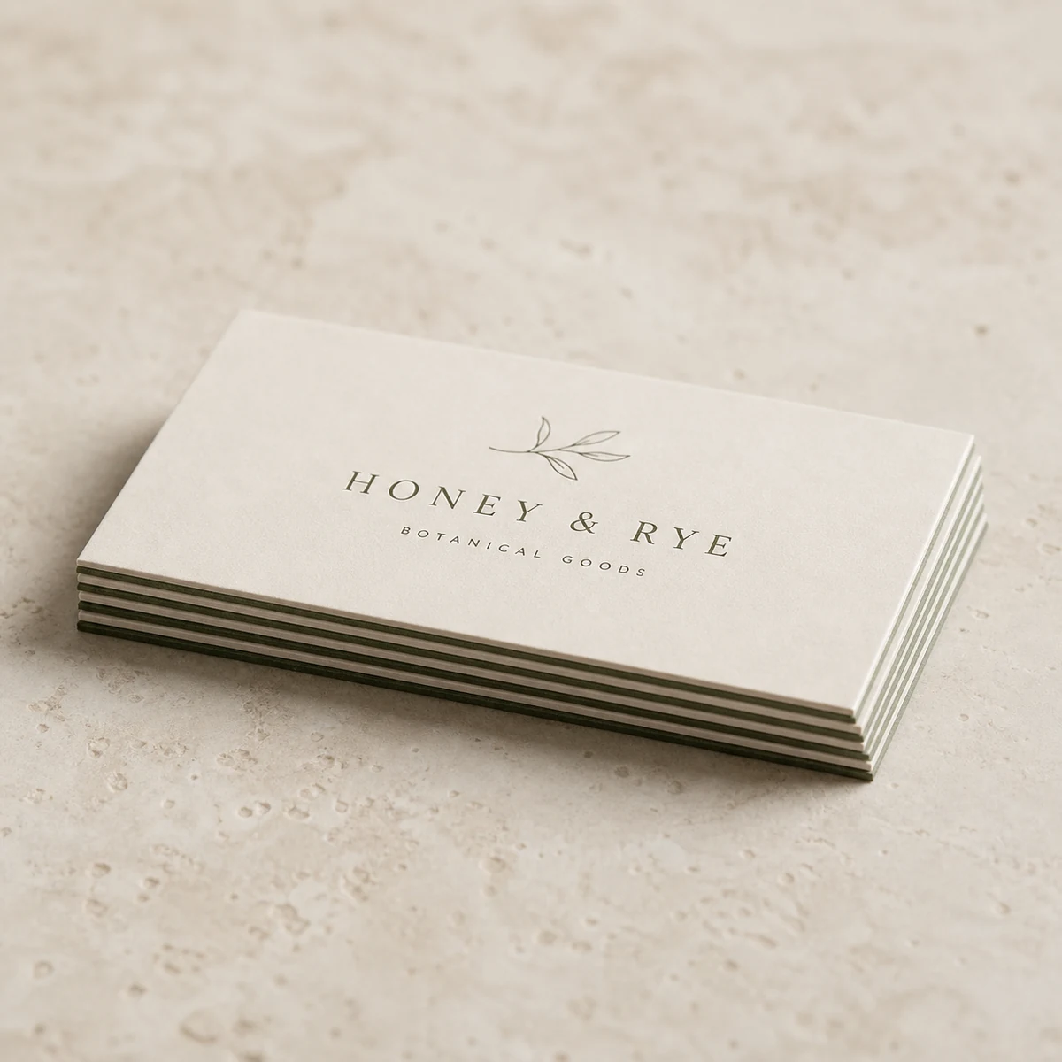 Overhead flat lay of a low stack of thin duplex business cards on light stone with the slim two-tone two-ply bonded cut edge visible, a cream face over a sage-green ply