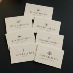 A fan of cream linen business cards with sharp black typography spread on a dark surface, clean fast-turnaround standard cards