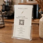 A DL printed menu in a clear acrylic counter holder on a cafe counter, a QR code in the lower third under a Scan for today's specials headline, warm cafe interior