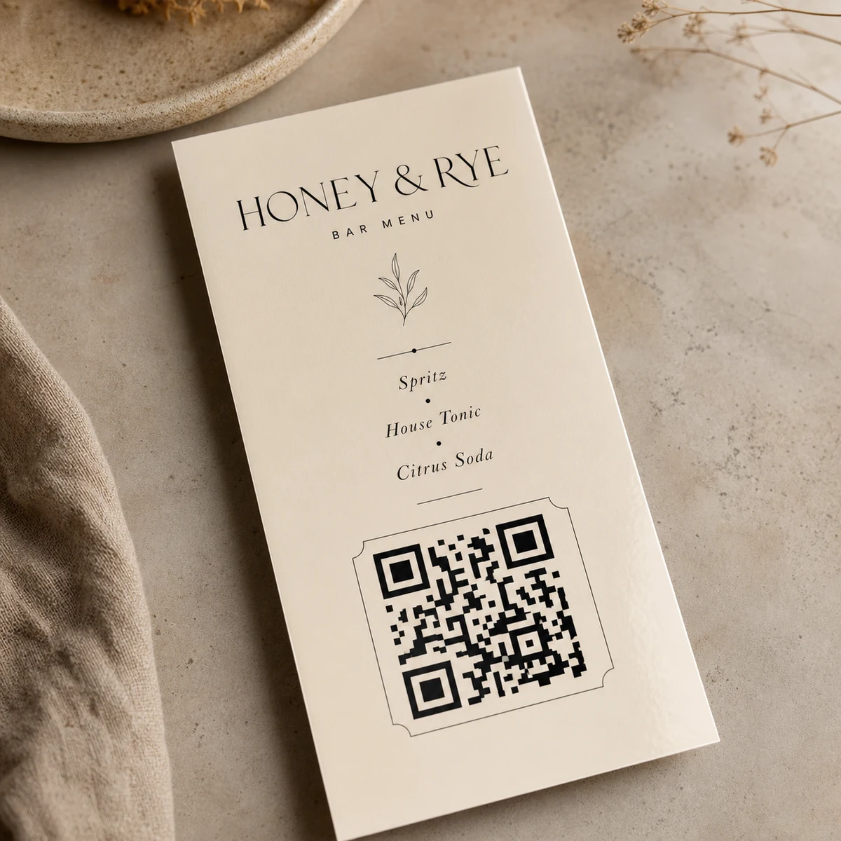 Overhead macro of a printed DL menu showing a crisp black-on-white QR code with a clean quiet-zone margin, dark ink on cream 300gsm stock, laminate sheen at the edge