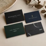Overhead flat lay of four dark velvet soft-touch business cards, black with white type, navy with gold, dark green, and charcoal with a flush spot-UV element, eucalyptus prop