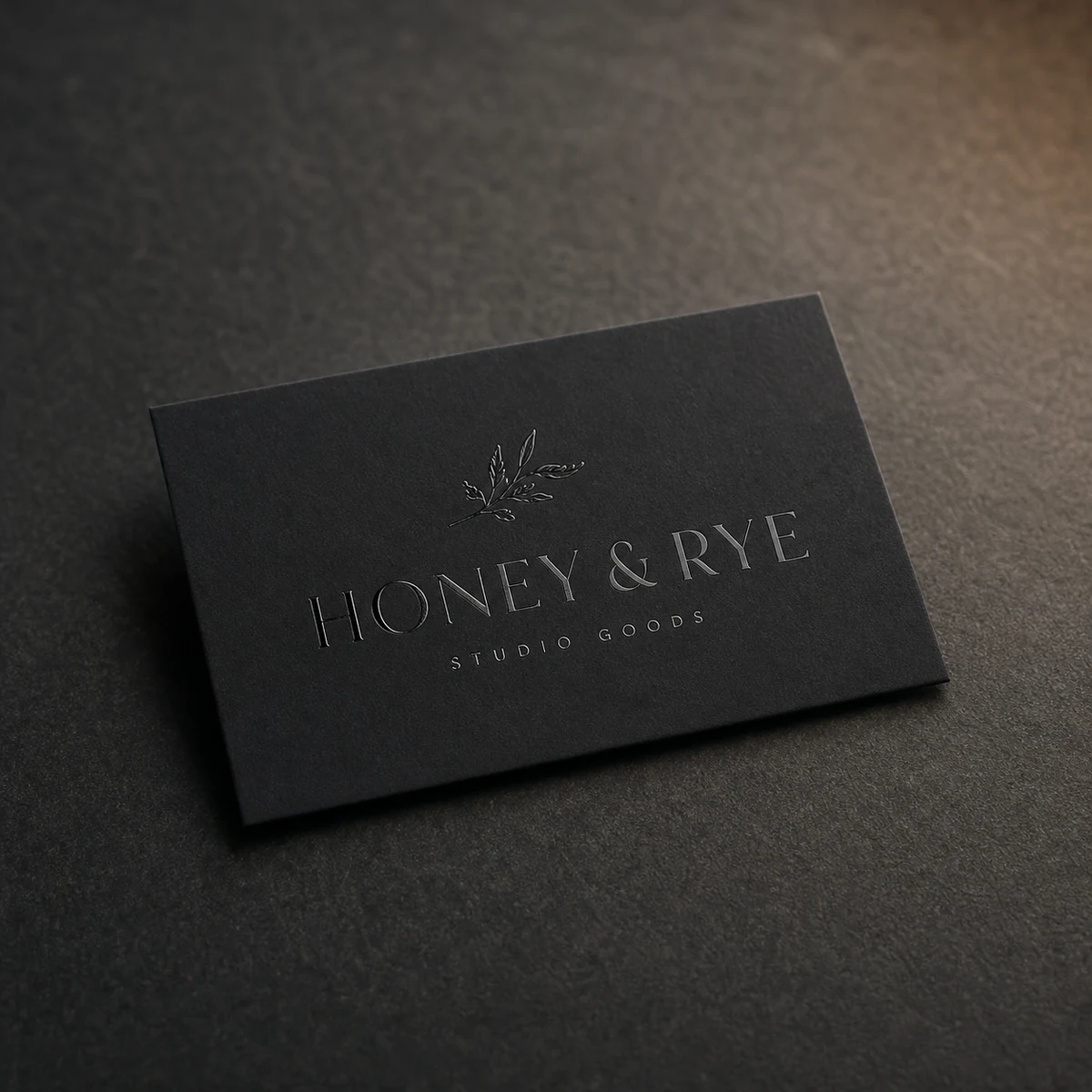 A black soft-touch business card with a tonal black-on-black spot-UV logo, the spot-UV a flush gloss sheen with zero relief against the matte velvet surface