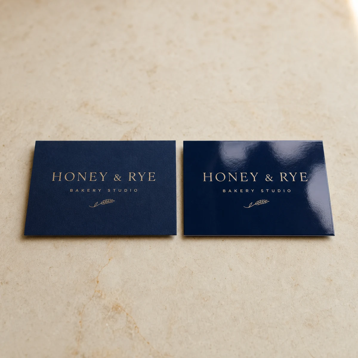 Two business cards side by side, one with a deep dead-matte velvet soft-touch laminate and one with standard gloss, showing the colour-depth difference, shot flat on a light surface