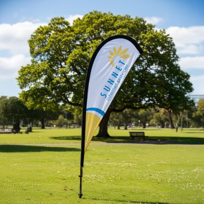 Custom-printed teardrop banner flag on a ground spike in a park, showing full-colour dye-sublimation branding