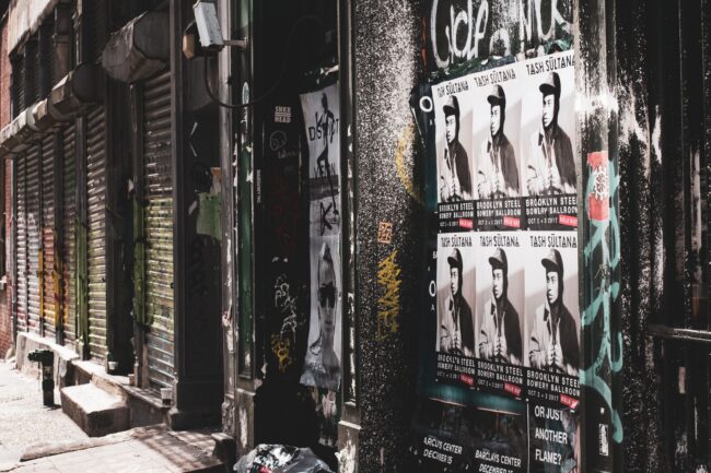 layered gig and event posters pasted on a street wall