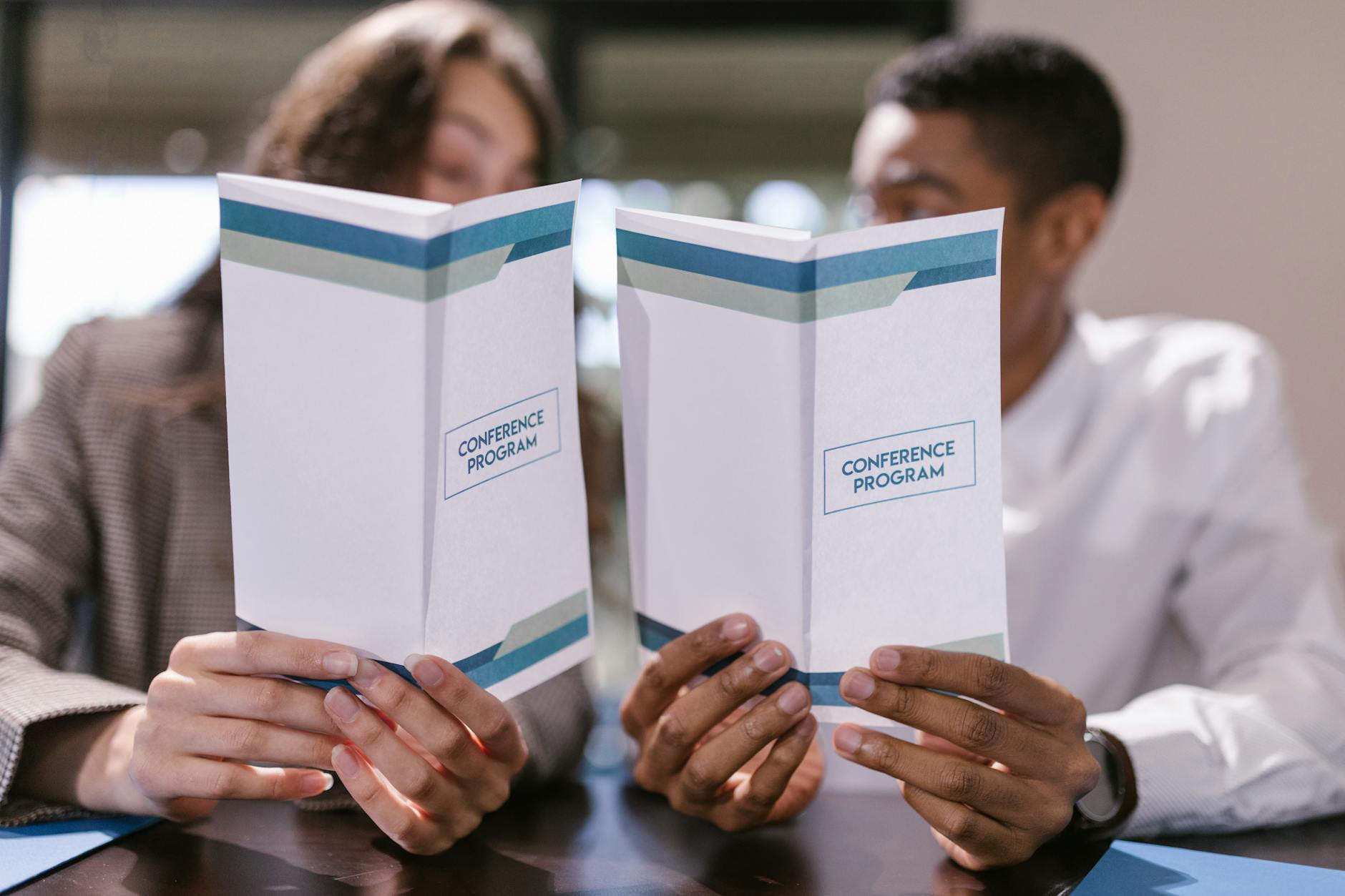 An open A5 conference program booklet on a table beside a name badge and a coffee cup, showing a two-column session timetable layout in