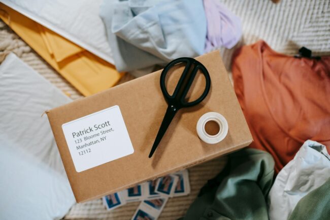 a row of white address labels printed with a business name and address, peeled from a sheet and applied to kraft paper padded bags on a
