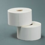 two rolls of blank white self-adhesive product labels stacked on a grey background