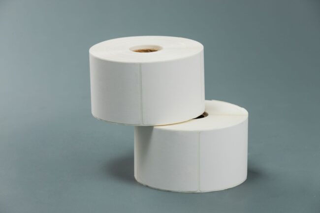 two rolls of blank white self-adhesive product labels stacked on a grey background
