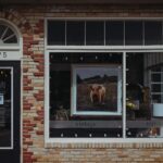 a small retail shopfront on an Australian high street showing a fascia sign above the door, window decals with business hours, and an