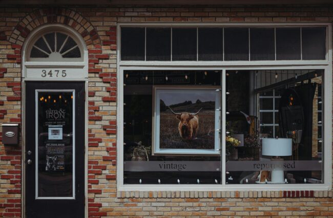 a small retail shopfront on an Australian high street showing a fascia sign above the door, window decals with business hours, and an
