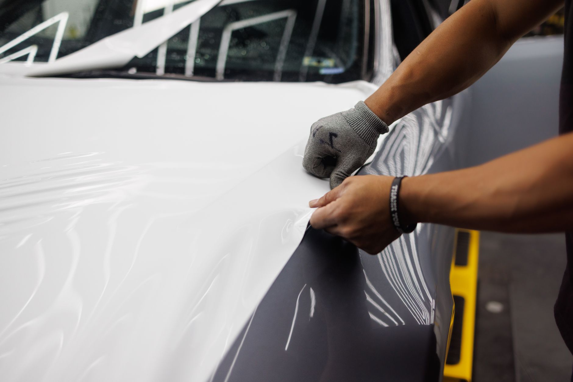 gloved hands smoothing a vinyl sheet onto a car panel