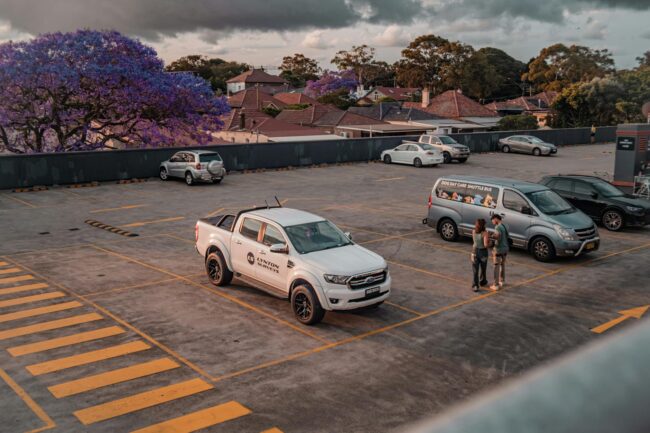 a white tradesman's ute parked on a suburban street with two professional car magnets on the doors, showing a plumbing business name, phone