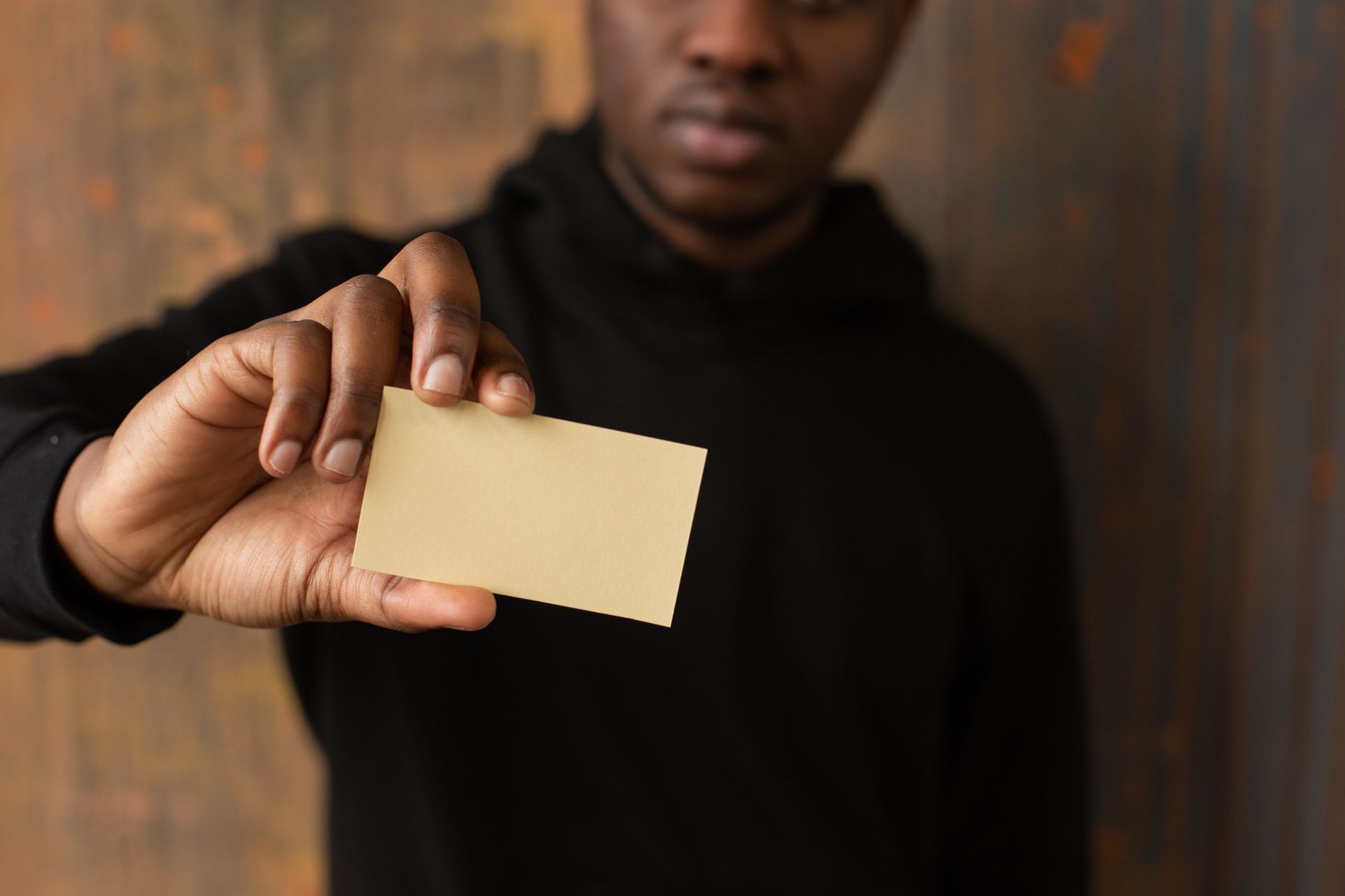a person in a black hoodie holding out a blank kraft business card toward the camera