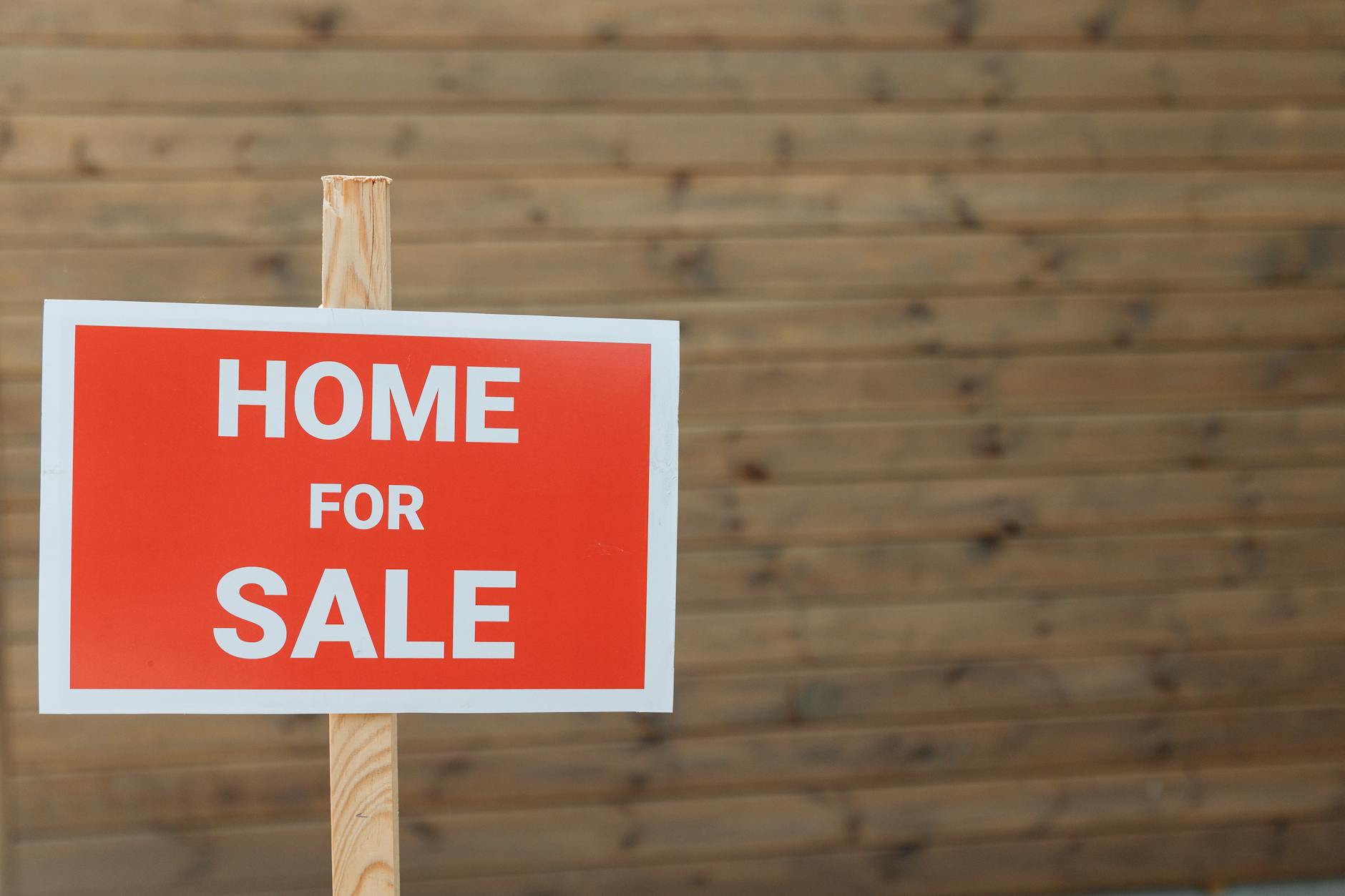 a red for-sale sign mounted on a post outside a property